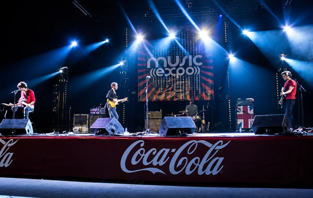 Concert sur la grande scène de Music Expo en 2009 : un groupe joue sous des projecteurs bleus, le logo Music Expo en fond de scène.