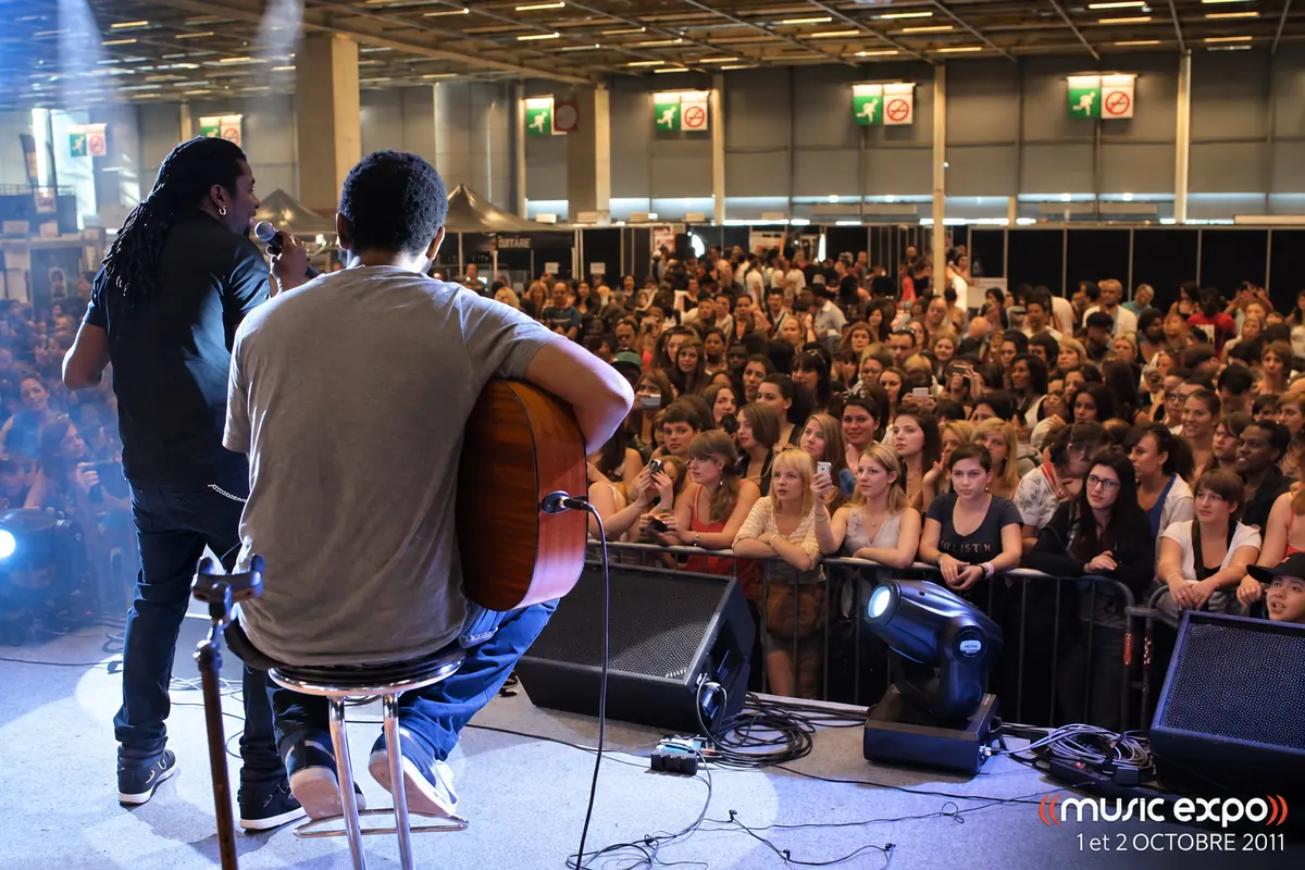 Vus depuis la scène, deux artistes font face à une foule dense venue les écouter.