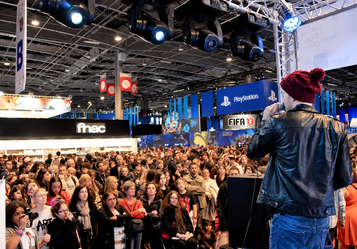 Un chanteur en bonnet fait face à une foule nombreuse, dans une halle d’exposition.